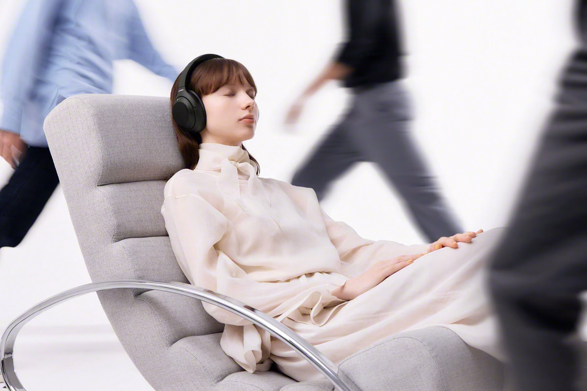 ผู้หญิงสวม Sony WH-1000XM4C สีดำนั่งพักท่ามกลางคนเดินผ่าน