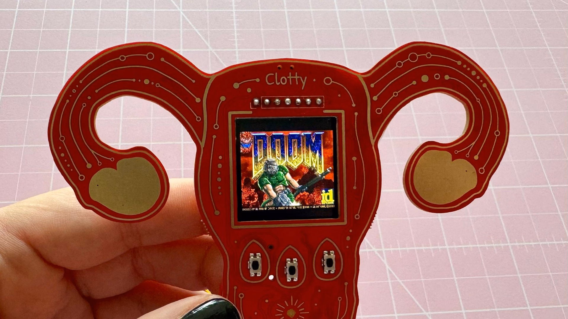 มือถือบอร์ด Clotty รูปมดลูกสีแดง จอกลางแสดงหน้าเกม DOOM