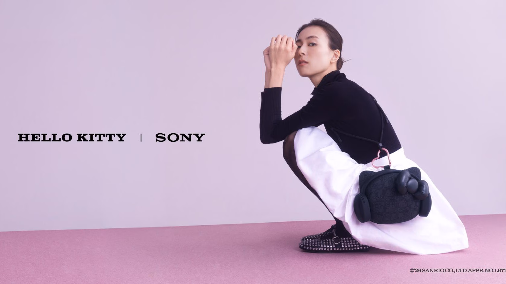 ผู้หญิงนั่งยองสะพายกระเป๋าทรงหัว Hello Kitty สีดำ ข้างโลโก้ HELLO KITTY | SONY